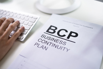 Business Continuity Plan BCP book with hand and computer keyboard