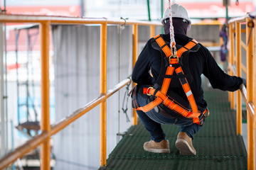 Construction worker in harness and safety line holding onto rail
